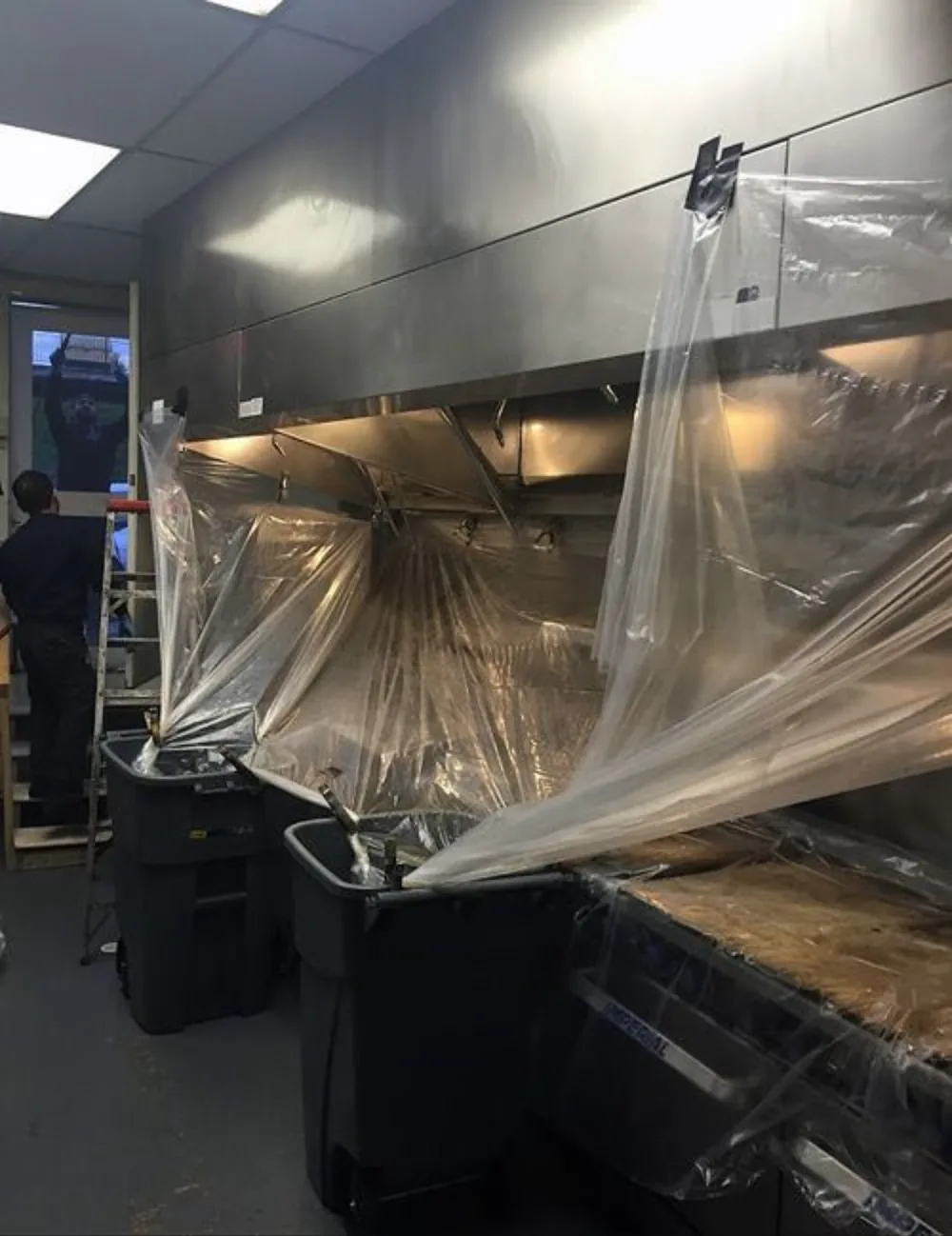 Hotte de cuisine professionnelle bâchée et bacs de récupération en place avant le dégraissage du caisson et des filtres